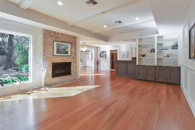 unfurnished living room featuring a brick fireplace, built in shelves, wood-type flooring, and beamed ceiling