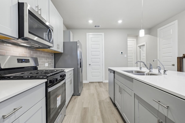 kitchen with backsplash, sink, hanging light fixtures, light wood-type flooring, and stainless steel appliances