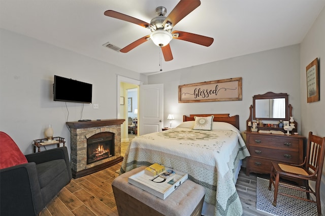 bedroom with hardwood / wood-style flooring, a stone fireplace, and ceiling fan