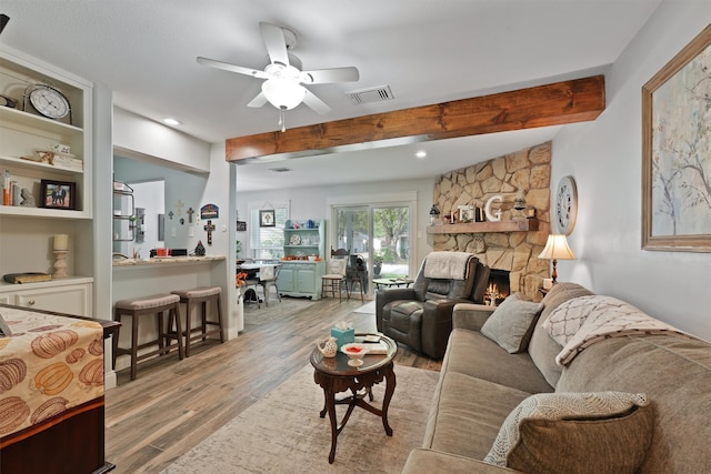 living room featuring a fireplace, beam ceiling, light wood-type flooring, and ceiling fan