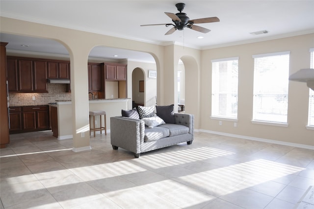 tiled living room with ceiling fan and crown molding