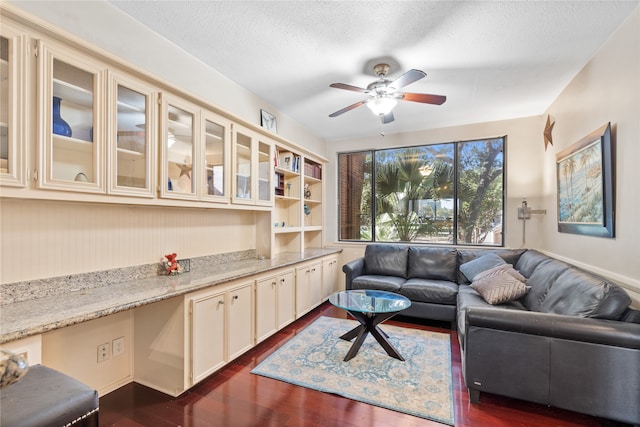 living room with a textured ceiling, ceiling fan, and dark wood-type flooring