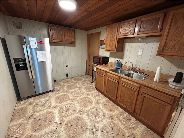 kitchen featuring stainless steel fridge with ice dispenser, sink, wooden ceiling, and wooden walls