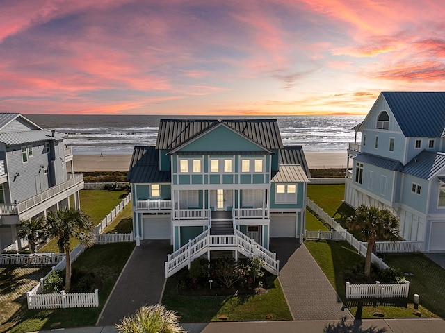 back house at dusk featuring a beach view, a water view, and a garage