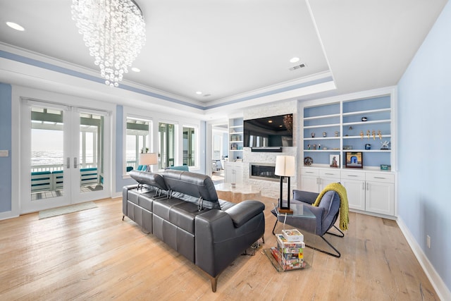 living room with french doors, a large fireplace, crown molding, an inviting chandelier, and light hardwood / wood-style floors