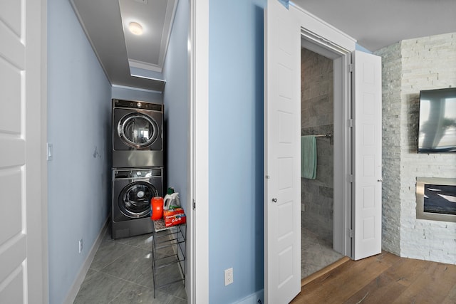 clothes washing area featuring stacked washer and clothes dryer, dark hardwood / wood-style flooring, crown molding, a fireplace, and tile walls