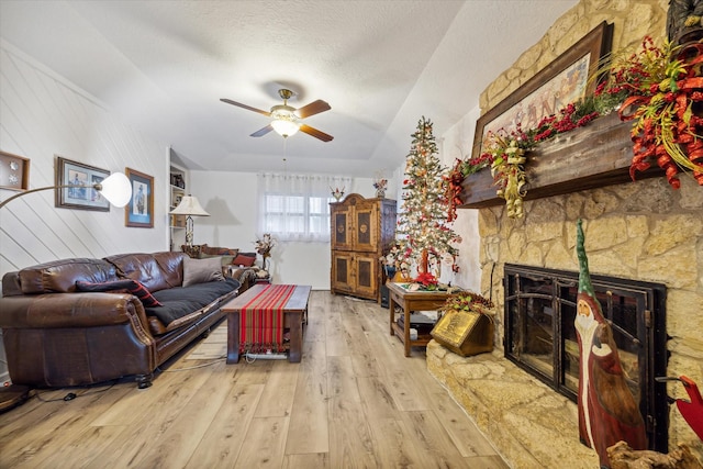 living room featuring wooden walls, ceiling fan, a textured ceiling, a fireplace, and light hardwood / wood-style floors