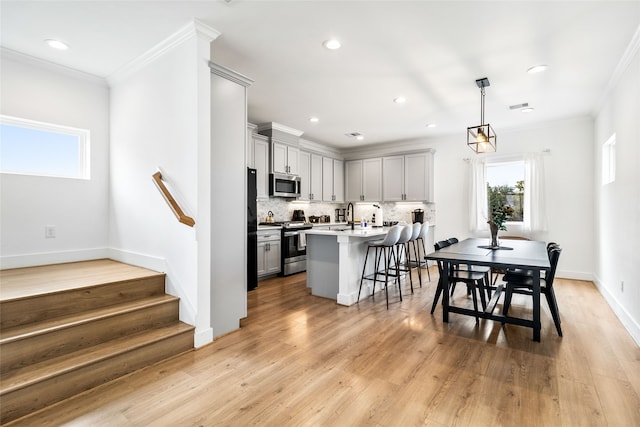 kitchen with a center island with sink, stainless steel appliances, decorative light fixtures, and light wood-type flooring