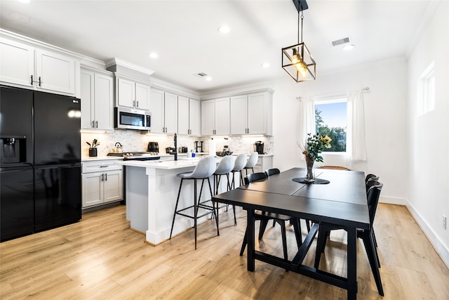 kitchen with a kitchen breakfast bar, light wood-type flooring, backsplash, black fridge with ice dispenser, and decorative light fixtures