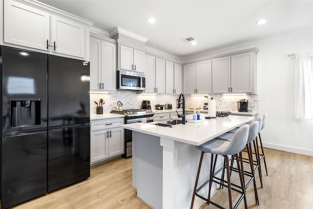 kitchen featuring an island with sink, a breakfast bar area, decorative backsplash, appliances with stainless steel finishes, and light wood-type flooring