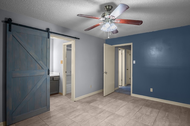 unfurnished bedroom with ceiling fan, a barn door, ensuite bathroom, and a textured ceiling