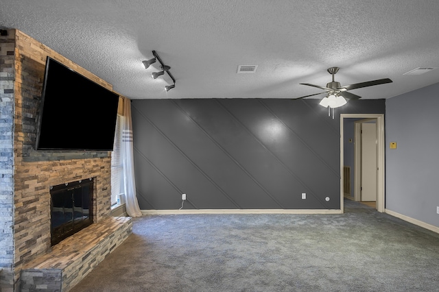 unfurnished living room featuring carpet, a textured ceiling, track lighting, and a brick fireplace