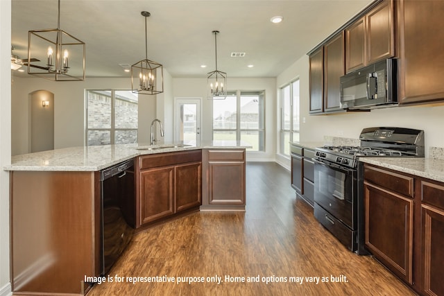 kitchen with pendant lighting, black appliances, a center island with sink, sink, and dark hardwood / wood-style flooring