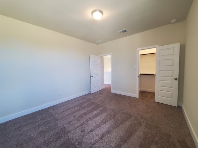 unfurnished bedroom with visible vents, baseboards, a closet, dark carpet, and a walk in closet