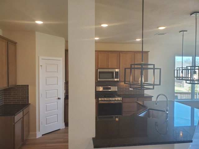 kitchen featuring dark countertops, visible vents, backsplash, appliances with stainless steel finishes, and a sink