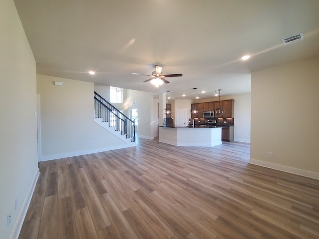 unfurnished living room featuring baseboards, visible vents, ceiling fan, stairway, and wood finished floors