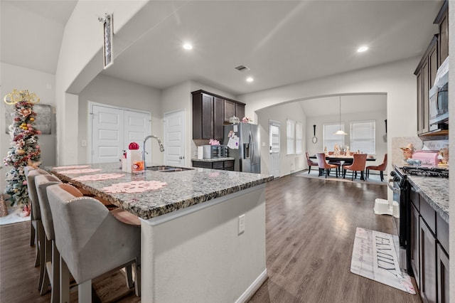 kitchen featuring light stone countertops, stainless steel fridge, black gas range oven, dark wood-type flooring, and sink