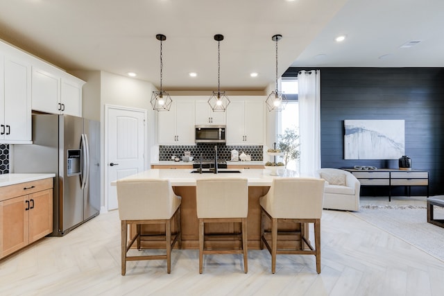 kitchen with white cabinets, decorative backsplash, an island with sink, and appliances with stainless steel finishes