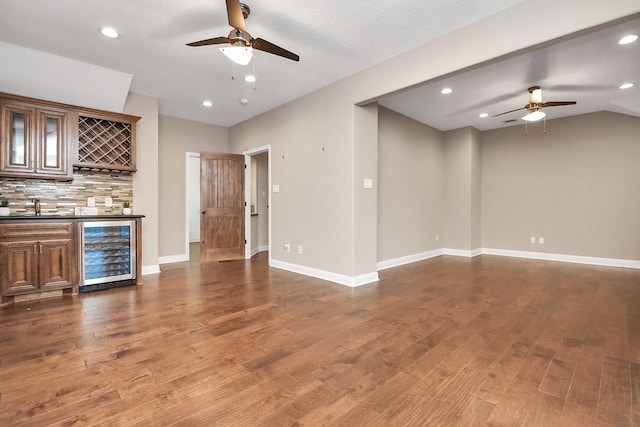 unfurnished living room with beverage cooler, ceiling fan, wet bar, hardwood / wood-style floors, and lofted ceiling