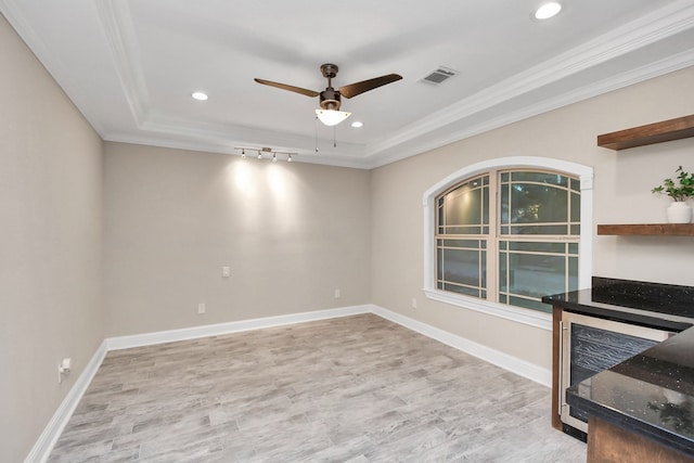 empty room with ceiling fan, rail lighting, crown molding, a tray ceiling, and light wood-type flooring