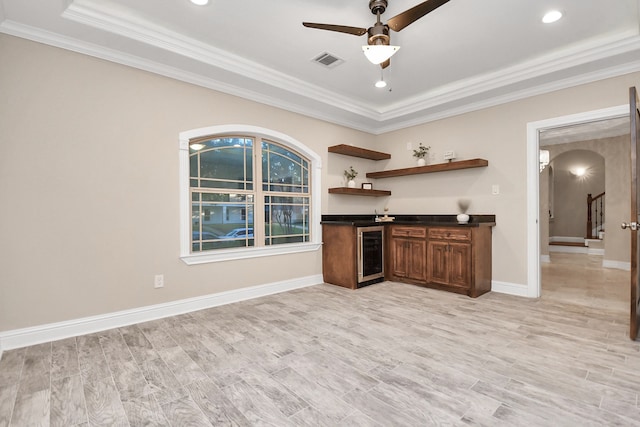 kitchen featuring light wood-type flooring, a tray ceiling, wine cooler, and crown molding