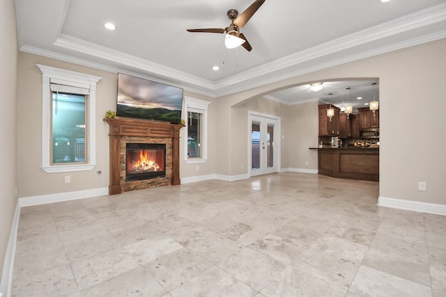 unfurnished living room featuring a fireplace, a raised ceiling, ceiling fan, and ornamental molding