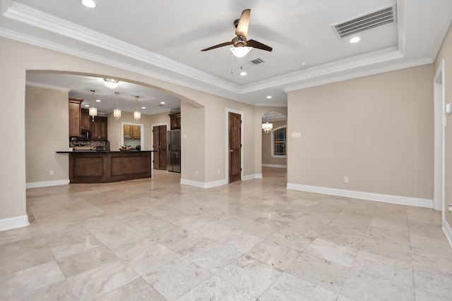 unfurnished living room with a tray ceiling, ceiling fan, and ornamental molding