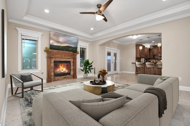 living room featuring a fireplace, a raised ceiling, ceiling fan, and crown molding