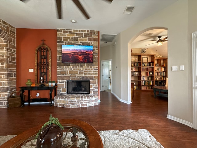 living room with dark hardwood / wood-style floors, a stone fireplace, and ceiling fan