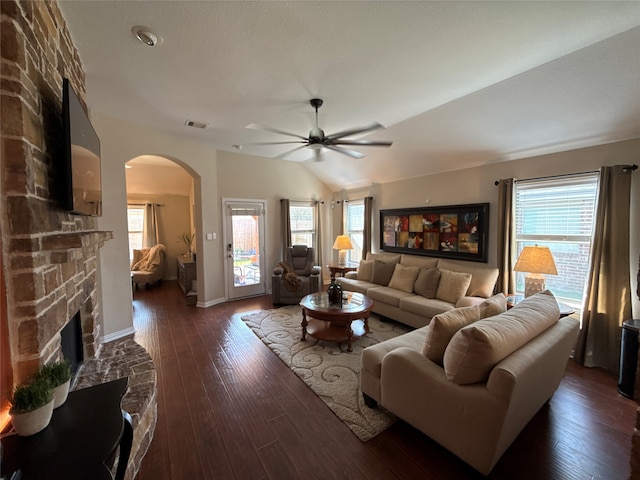 living room with ceiling fan, a stone fireplace, dark wood-type flooring, and vaulted ceiling