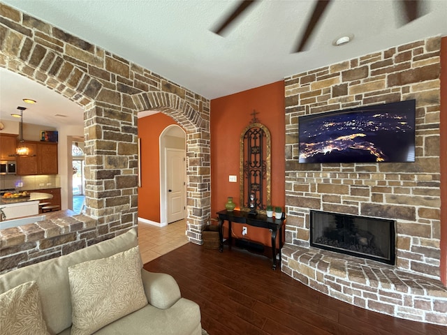 living room with hardwood / wood-style floors, a textured ceiling, and a stone fireplace