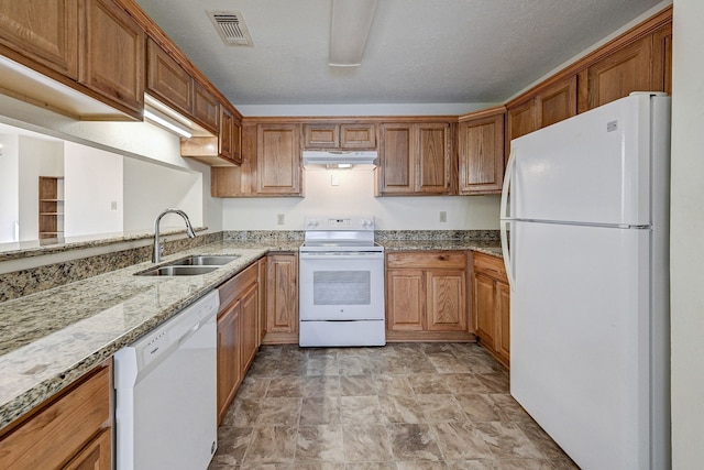 kitchen with a textured ceiling, light stone countertops, white appliances, and sink