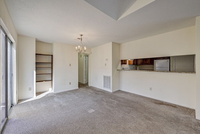 unfurnished living room featuring a chandelier, light carpet, and a textured ceiling