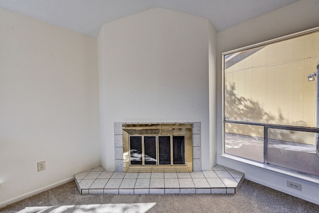 interior space with a tiled fireplace, carpet floors, and vaulted ceiling