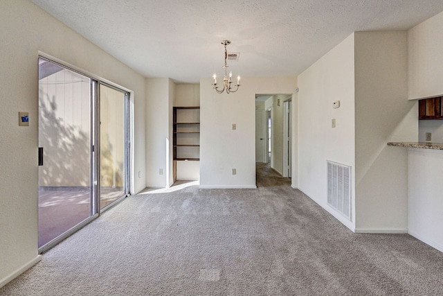 carpeted empty room with a textured ceiling and a chandelier