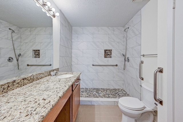 bathroom featuring vanity, a tile shower, a textured ceiling, and tile patterned flooring