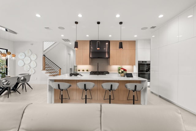 kitchen featuring a kitchen breakfast bar, a spacious island, wall chimney range hood, decorative light fixtures, and white cabinetry