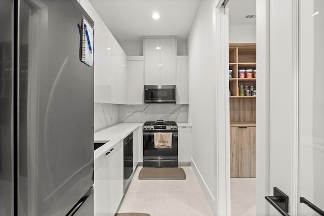 kitchen with tasteful backsplash, light stone counters, light tile patterned flooring, white cabinets, and appliances with stainless steel finishes