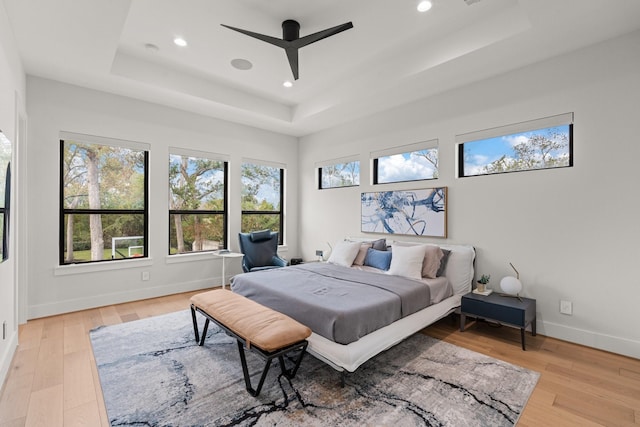 bedroom featuring ceiling fan, light hardwood / wood-style flooring, and a tray ceiling