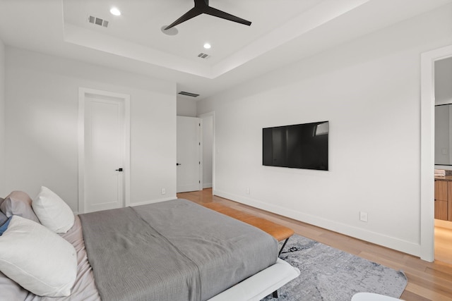 bedroom featuring a raised ceiling, connected bathroom, ceiling fan, and light wood-type flooring