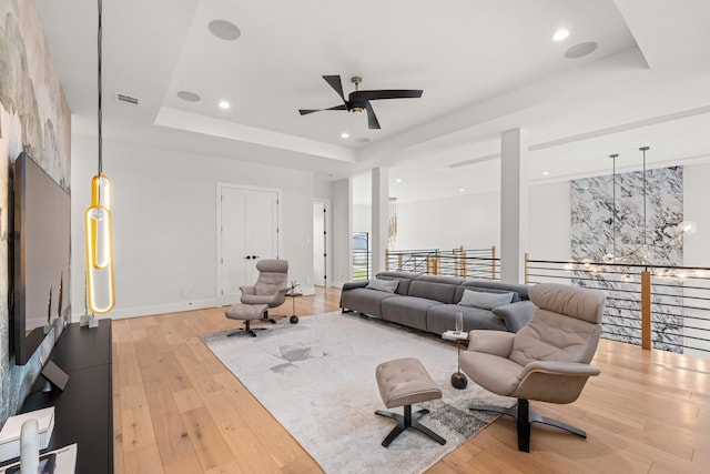 living room with a raised ceiling, ceiling fan, and light hardwood / wood-style floors