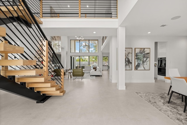 staircase with concrete flooring, a towering ceiling, and a notable chandelier