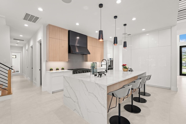 kitchen featuring white cabinets, light brown cabinets, hanging light fixtures, and wall chimney exhaust hood