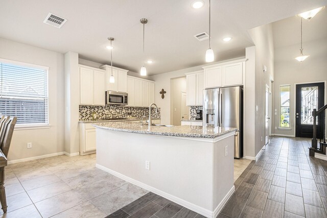 kitchen with appliances with stainless steel finishes, a kitchen island with sink, white cabinets, and decorative light fixtures