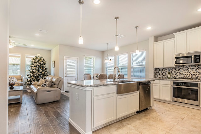 kitchen featuring appliances with stainless steel finishes, sink, pendant lighting, a center island with sink, and white cabinetry