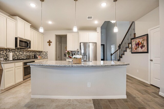 kitchen with a kitchen island with sink, stainless steel appliances, light stone countertops, decorative backsplash, and decorative light fixtures
