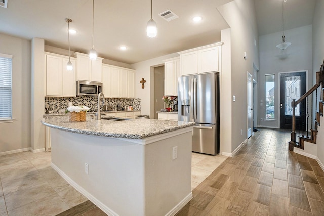 kitchen featuring sink, white cabinetry, hanging light fixtures, stainless steel appliances, and a kitchen island with sink