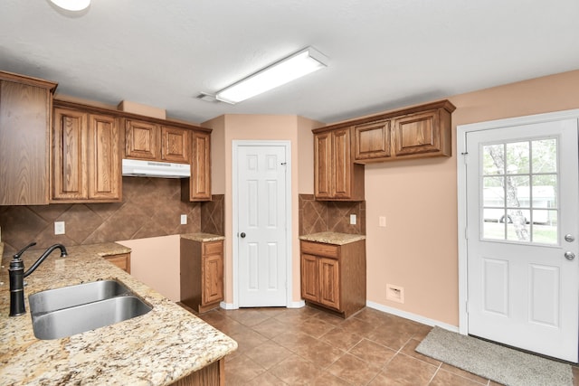 kitchen with light tile patterned floors, tasteful backsplash, light stone counters, and sink