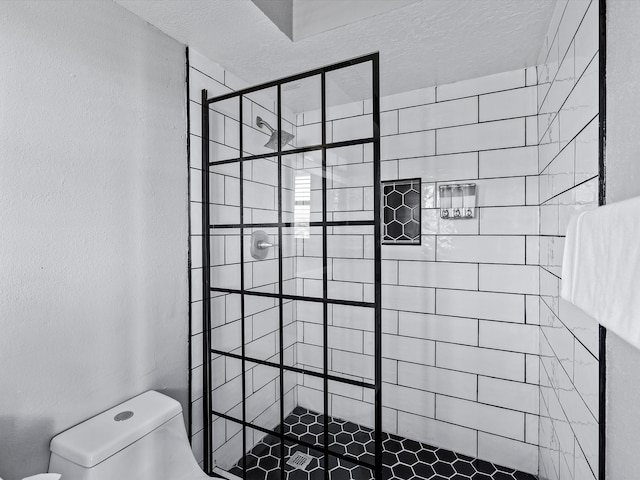 bathroom featuring toilet, a tile shower, and a textured ceiling