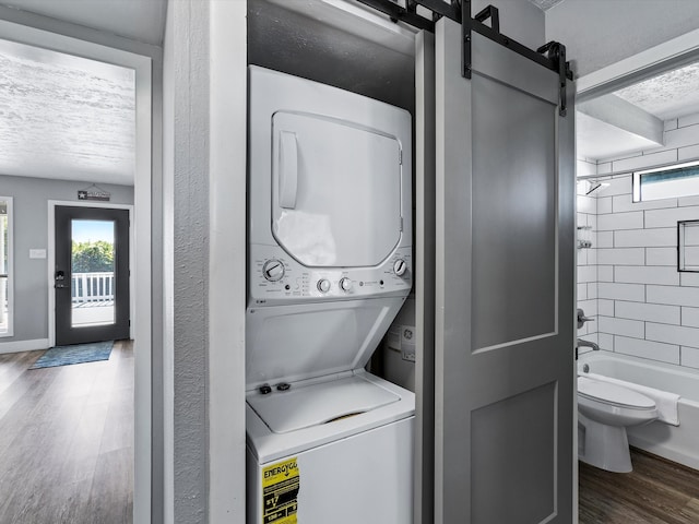 laundry room featuring plenty of natural light, a barn door, dark hardwood / wood-style floors, and stacked washer and clothes dryer